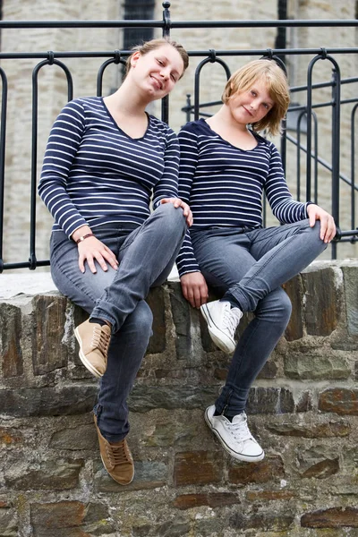 Two teenage girls sitting side by side, wearing the same dress and smiling