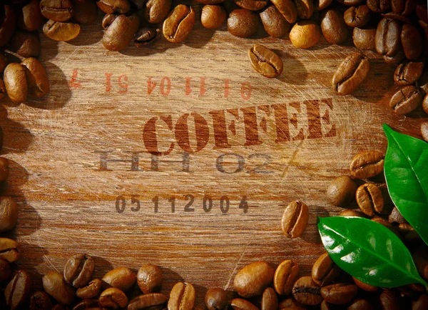 新鲜的烤咖啡豆 内嵌一个印有 Coffee 字样的老式木板 以及角落里装有两片新鲜绿叶的豆子的装运编号 — 图库照片