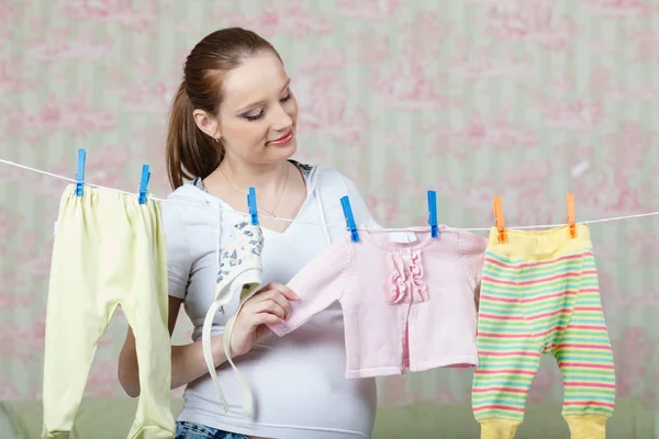 妊娠中の女性がロープで家に子供服をぶら下げて — ストック写真