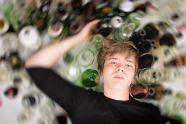 young man with short blond hair lying on the floor and is surrounded by many empty beer and schnapfsflaschen,upper perspective. clipart