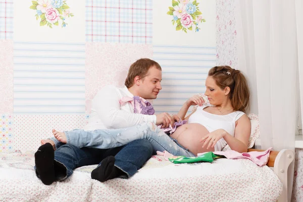 Lycklig Gravid Familj Med Barnkläder Sitta Sängen Hemma — Stockfoto