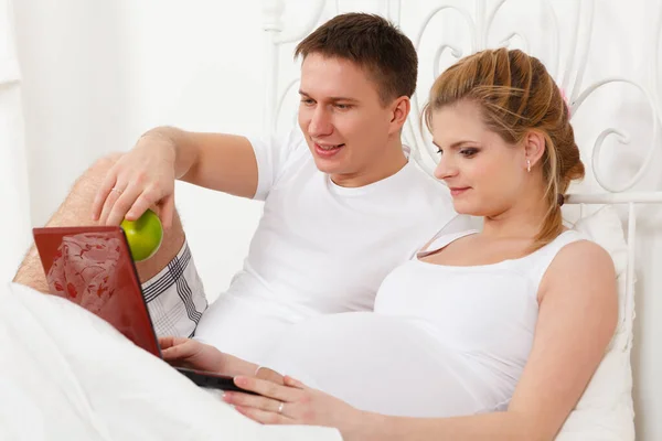 Szczęśliwa Rodzina Ciąży Notatnikiem Leży Łóżku Domu — Zdjęcie stockowe