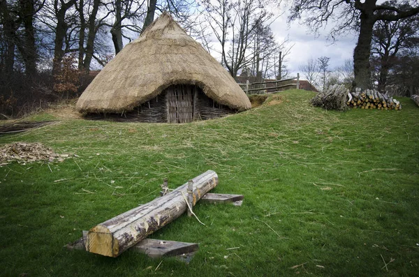 A replica of an iron age round house with log in foreground