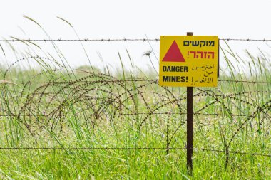 Protective barbed wire fence and warning sign around a minefield on Golan Heights clipart
