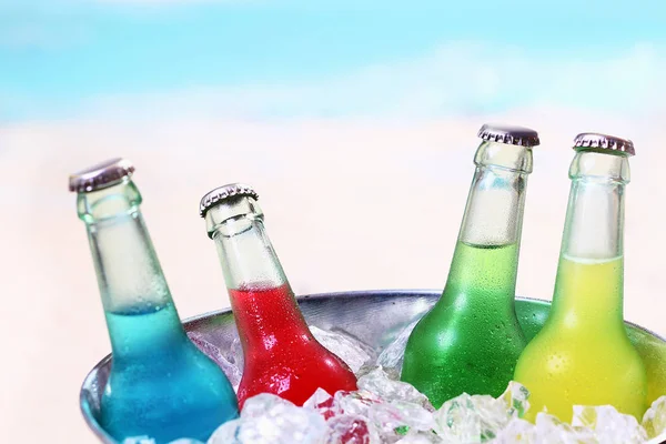 Colourful chilled soda drinks in unlabeled glass bottles standing in a metal container of crushed ice cubes for a summer party