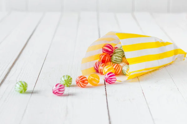 Yellow striped candy bag spilling its candies over a white wooden table
