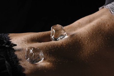 the naked belly of a young woman with navel,water droplets and ice cubes against black background. clipart