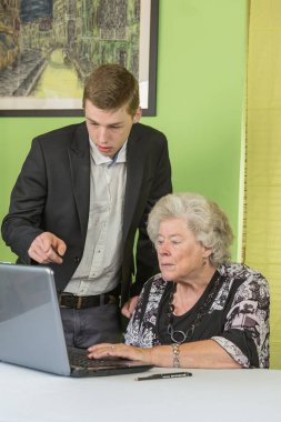 senior lady and young man work together on laptop. clipart