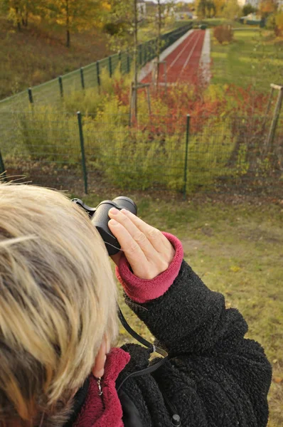 成熟的女人用双筒望远镜看森林边缘 — 图库照片
