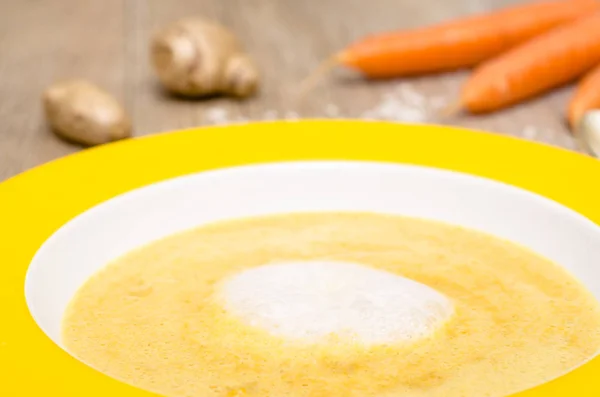 foam of coconut milk to soup with carrots in a plate