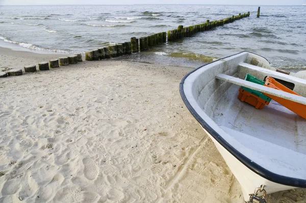 frontal wide shot of a small fishing boat on the white sand beach with groyne in the background