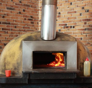 Wood fired pizza oven with flame against brick wall clipart