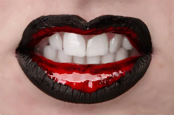 close-up of a pretty female mouth. the girl has brightly painted lips in black and red and shows her teeth.