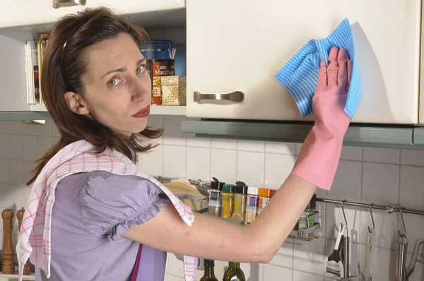 adult housewife standing in her bright kitchen and cleans with rubber gloves and cleaning cloths.