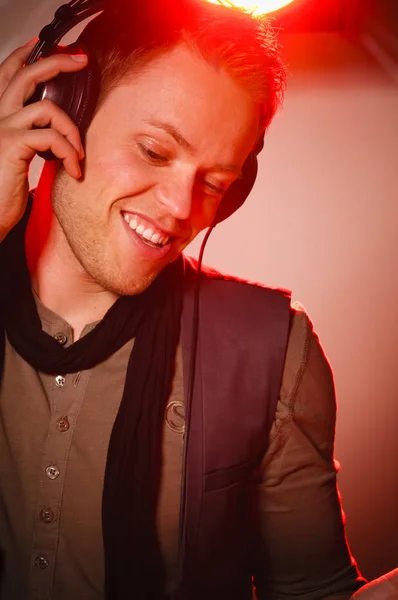 young man listens to hot music through headphones and makes a boisterous facial expression. in the background a disco spotlight throws red backlight.