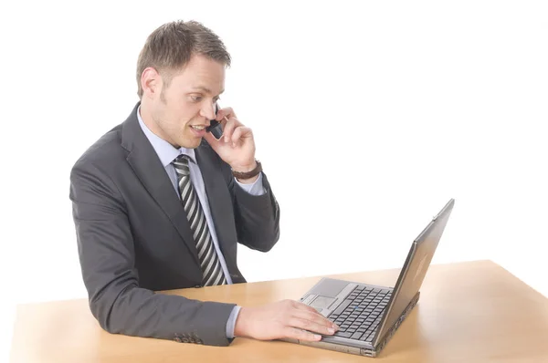 スーツとネクタイを着た若いビジネスマンが机に座りノートパソコンで仕事をしています 彼は顧客に電話して取引を締結する 白い背景の前に隔離され — ストック写真