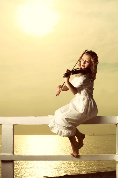 the blonde girl music lover on pier with a violin at sunset or sunrise. love of music concept.