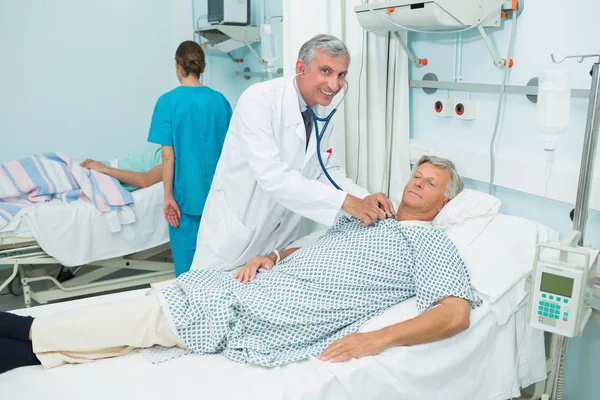 病院のベッド病棟で男性患者を会計検査をする男性医師の笑顔 — ストック写真