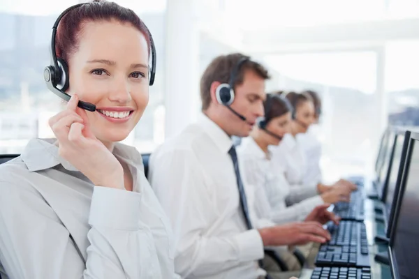 Smiling call center agent with her colleagues behind her