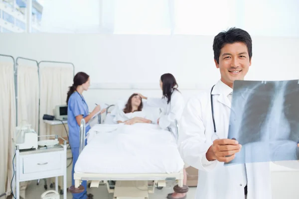 Doctor Smiling Holds Ray Scan While His Colleagues Treating Patient — Stock Photo, Image