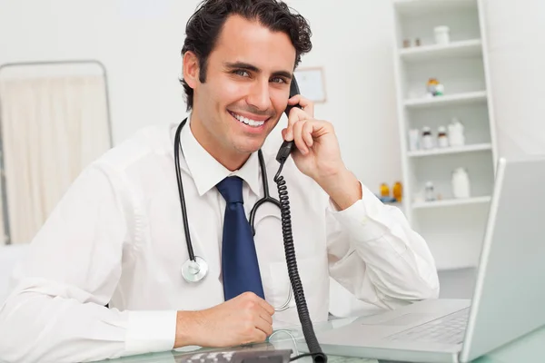 Smiling Doctor Sitting His Desk While Being Phone —  Fotos de Stock