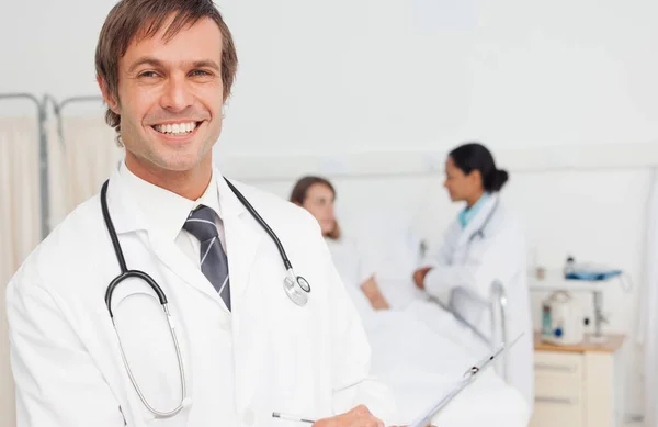 Χαμογελώντας Γιατρός Κρατώντας Ένα Πρόχειρο Ενώ Στέκεται Ένα Δωμάτιο Νοσοκομείου — Φωτογραφία Αρχείου