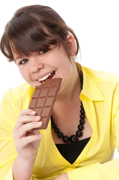 長い髪と黄色のブラウスを持つ10代の女の子は白を背景にしたチョコレートを楽しみながら食べました — ストック写真