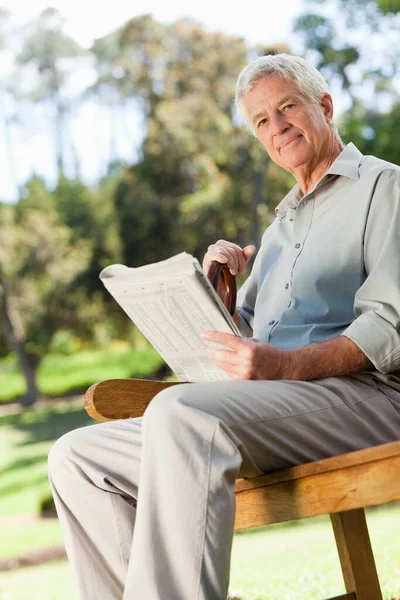 An old man is sitting down holding a newspaper and looking at the camera