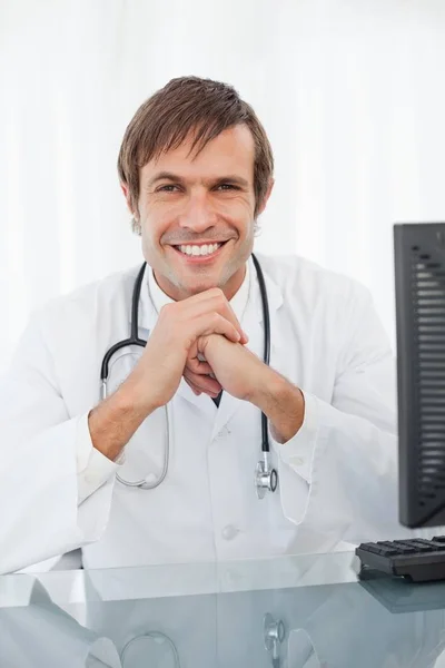 Uśmiechnięty Doktor Siedzący Przy Biurku Rękami Podbródku — Zdjęcie stockowe