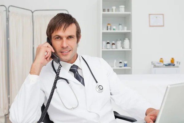 Uśmiechnięty Lekarz Rozmawiający Przez Telefon Podczas Pracy Nad Laptopem — Zdjęcie stockowe