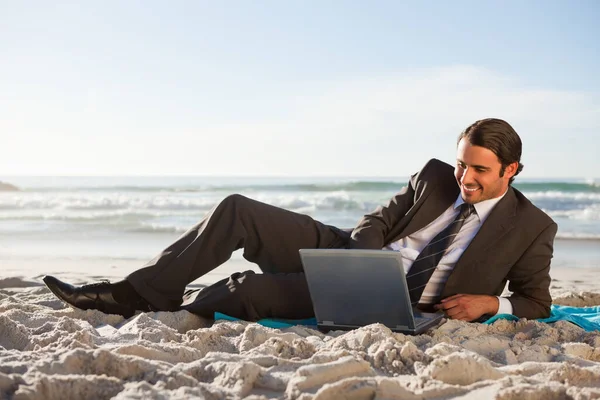 微笑的商人一边躺在沙滩上一边 一边用笔记本电脑 — 图库照片