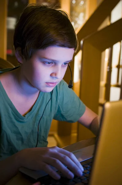 waist-view of a young male teenagers at the table on a laptop looking in a darkened environment