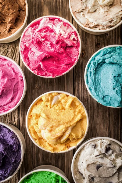 Overhead view of a selection of colorful tubs of Italian ice cream in a variety of flavors on a rustic wooden surface for a delicious summer dessert