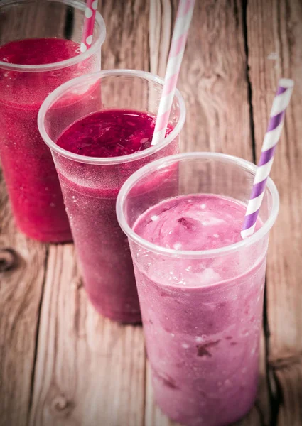 Healthy delicious trio of different berry smoothies with low fat yogurt arranged in a diagonal row, high angle view on an old rustic wooden background