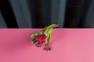 a plastic toy tyrannosaurus rex eating a bouquet of red roses on a vibrant green curtain and pink background. Minimal funny and quirky pop still life photography clipart