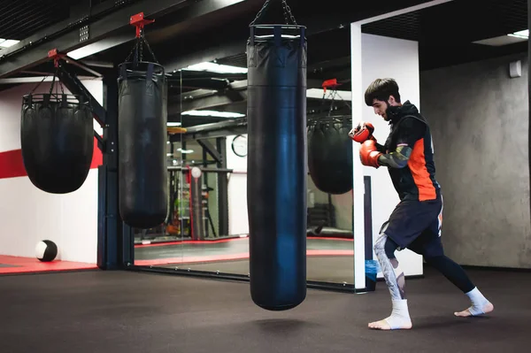プロのムエタイ戦闘機 トレーニング中の男性ボクサースポーツウェア スポーツホールでの練習 パンチングバッグでのトレーニング 打撃をうながす — ストック写真