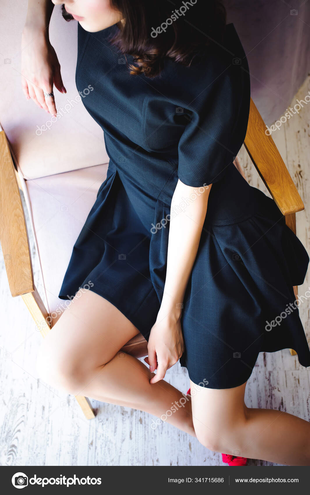 黒のエレガントなドレスで長い脚を持つ若い魅力的な女性は 部屋のインテリアで窓の近くの椅子に座っている — ストック写真 ©