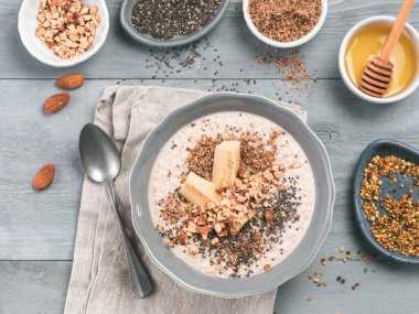 Overnight oats in bowl and ingredients - banana, LSA, chia seeds, almond, honey and pollen on gray wooden table background. Healthy breakfast oatmeal recipe idea. Top view clipart
