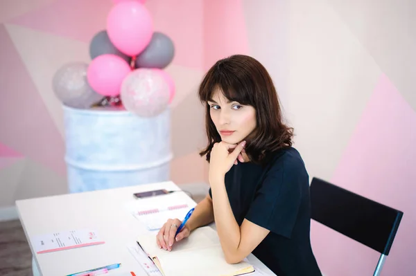 一个漂亮的女商人在笔记本上做笔记的肖像 拿着一支笔 坐在粉红办公室的工作场所 — 图库照片