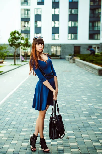 長い髪の長い脚を持つ若い魅力的な女性は 彼の手に黒い袋と剣ベルトで青エレガントなドレスで ヨーロッパの近代的な中庭 暖かい夏の日に散歩 — ストック写真