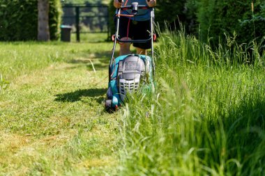 Man cutting grass with  an electro lawnmower in his garden. clipart