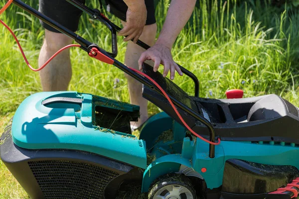 Close up on man emptying the catch basket of an electro lawnmower in his garden.