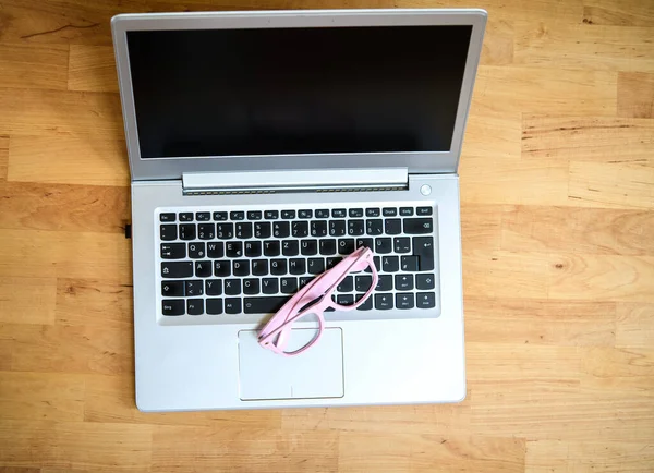 laptop with pink glasses on wooden ground