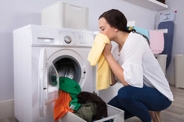 洗濯機近くの清潔な黄色の布を嗅ぐ若い女性の側面図 — ストック写真