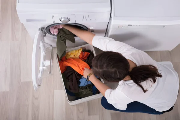 洗濯機でバスケットから服をロードする若い女性の高架ビュー — ストック写真