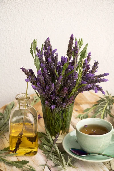 on a table is a vase of fragrant lavender flowers and a cup of fresh lavender tea and a bottle of lavender oil