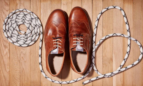 Fashion shoes, new brown polished classic shoes for men and rope lies on a wooden background. Top view.