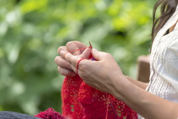 在模糊的背景前用红色羊毛 针织品钩针的女人的手 — 图库照片