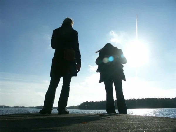 一个男人和女人背着背包站在海滩上看着摄像机的轮廓 — 图库照片
