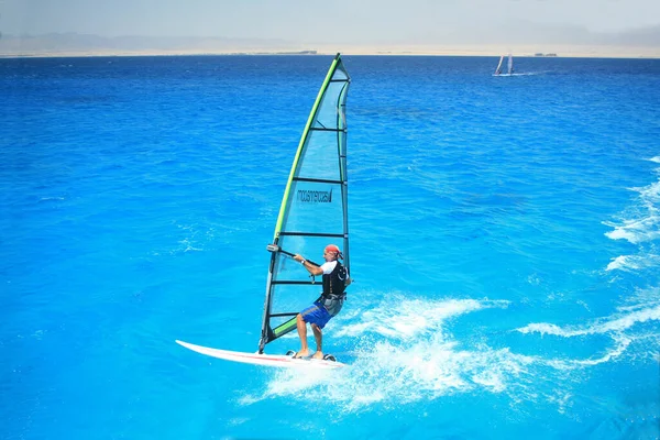 青いシャツを着た男が海のサーフボードに飛び乗り — ストック写真